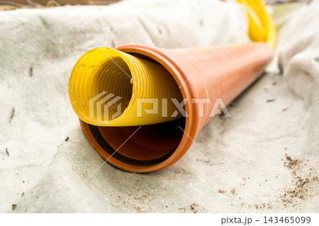 A close look at two different drainage pipes, one yellow and the other brown, lying on the ground at a construction site. 143465099