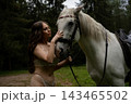 Woman in lace lingerie stroking a white horse in a clearing 143465502