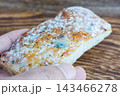 A hand holding a slice of moldy bread over a wooden background 143466278