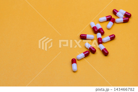 Red and white capsules scattered on a yellow surface, oral pharmacy products associated with medication use in older adults, healthcare budgeting and the pharmaceutical industry. Red and white capsules scattered on a yellow surface, oral pharmacy products associated with medication use in older adults, healthcare budgeting and the pharmaceutical industry. 143466782