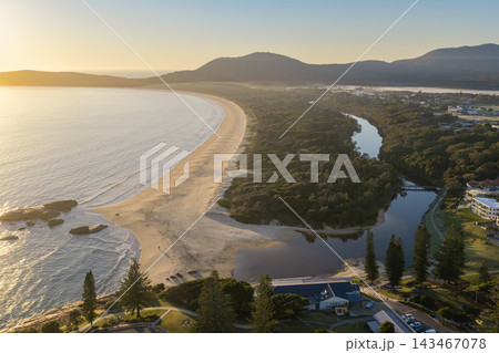 Aerial view of Front Beach and Saltwater Creek meeting the ocean, with a long sandy shoreline, coastal vegetation and a small bridge. Town buildings border the creek Aerial view of Front Beach and Saltwater Creek meeting the ocean, with a long sandy shoreline, coastal vegetation and a small bridge. Town buildings border the creek 143467078