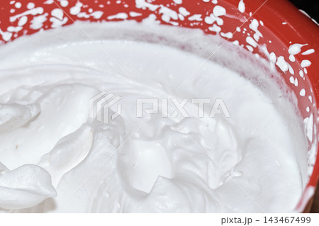 Close-up of freshly whipped white cream inside a bright red mixing bowl 143467499