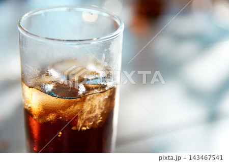Close-up of a tall glass filled with cold cola and ice cubes on table 143467541