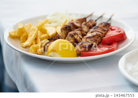 Grilled pork souvlaki skewers served on a white plate with french fries and tomatoes 143467555