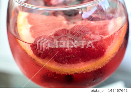 Close-up view of a refreshing pink gin cocktail garnished with fresh raspberries and citrus slices Close-up view of a refreshing pink gin cocktail garnished with fresh raspberries and citrus slices 143467641
