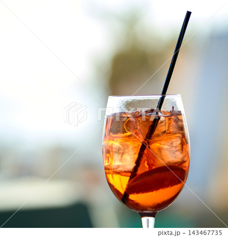 Close-up of a refreshing orange spritz cocktail with ice cubes and a black straw 143467735