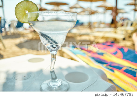 Close-up of a refreshing margarita cocktail served with lime on a beach table Close-up of a refreshing margarita cocktail served with lime on a beach table 143467785