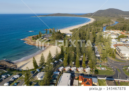 Aerial view of Horseshoe Beach beside a campground shaded by tall trees, with Front Beach curving around the bay in the background. Rocky headlands, waterfront buildings and coastal woodland border 143467878