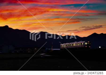 燃えるような夕焼けと山並みを走る小さな列車 143471265