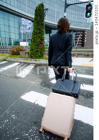 キャリーバッグを引くいて横断歩道を渡る女性 キャリーバッグを引くいて横断歩道を渡る女性 143472331