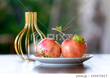 Indoor still life of fresh pomegranates on plate next to gold vase Indoor still life of fresh pomegranates on plate next to gold vase 143473817