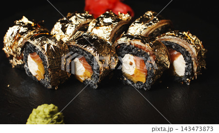 Luxury sushi rolls with black rice, salmon, cream cheese, mango, and edible gold leaf on a dark background 143473873
