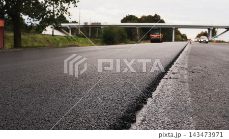 Asphalt paving work in progress on a highway with a fresh layer of road surface and a steam roller in the background Asphalt paving work in progress on a highway with a fresh layer of road surface and a steam roller in the background 143473971