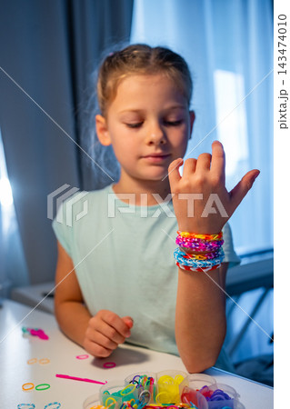 Smiling girl proudly shows colorful handmade rubber band bracelets on her wrist. Creative hobby builds confidence, independence and a sense of achievement while developing fine motor skills 143474010