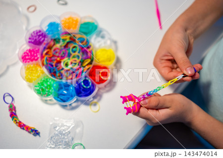 Child makes a bracelet from colorful rubber bands using a mini loom at home. Creative activity helps develop fine motor skills, hand eye coordination and concentration through play Child makes a bracelet from colorful rubber bands using a mini loom at home. Creative activity helps develop fine motor skills, hand eye coordination and concentration through play 143474014