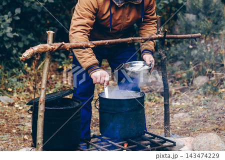 Tourist cooking camping food picnic on campfire kitchen, person put cream soup Tourist cooking camping food picnic on campfire kitchen, person put cream soup 143474229
