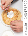 Man spreads sour cream topping on flat round pancake, breakfast morning in cafe 143474790