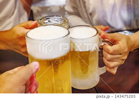 居酒屋でビールのジョッキを傾けて乾杯する手元 居酒屋でビールのジョッキを傾けて乾杯する手元 143475203