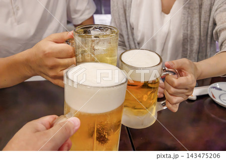 居酒屋でビールのジョッキを傾けて乾杯する手元 143475206