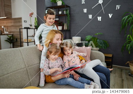 Mother looks at a book and reads a story to her daughters Mother looks at a book and reads a story to her daughters 143479065