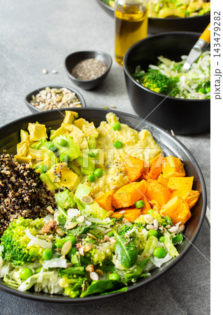A quinoa bowl is arranged with roasted pumpkin, hummus, and a fresh salad. Plates are set on a table with utensils. Sunshine comes through the window A quinoa bowl is arranged with roasted pumpkin, hummus, and a fresh salad. Plates are set on a table with utensils. Sunshine comes through the window 143479282