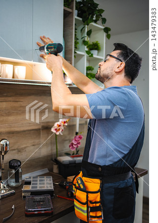 Man installing kitchen cabinet using cordless drill 143479383