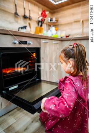 Little girl looking at food baking in oven in domestic kitchen Little girl looking at food baking in oven in domestic kitchen 143479465