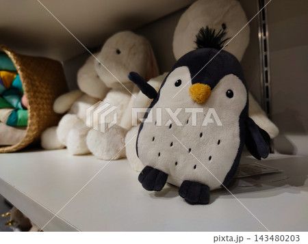 Cute black and white plush penguin soft toy with tuft of hair sitting on a white store shelf. 143480203