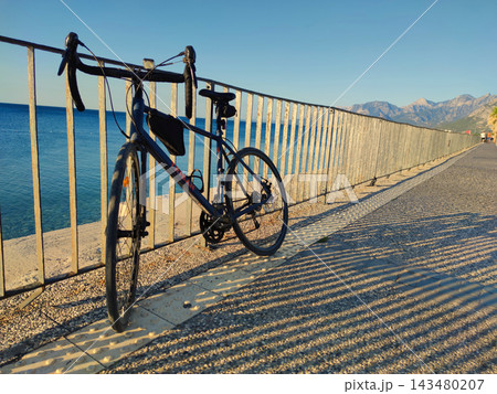 Dark Blue Triban Road Bike Leaning against Metal Fence on Coastal Promenade at Sunset. 143480207