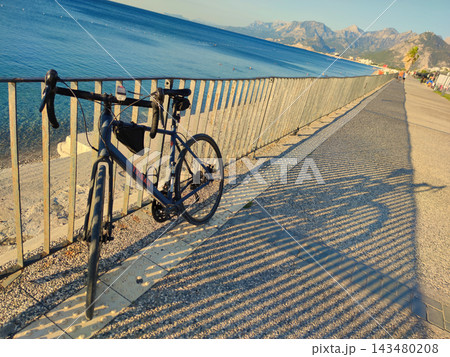 Dark Blue Triban Road Bike Leaning against Metal Fence on Coastal Promenade at Sunset. 143480208