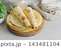 Stack of lavash or chapati flatbreads on a wooden cutting board, with a jar of flour, fresh basil 143481104