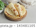 Stack of lavash or chapati flatbreads on a wooden cutting board, with a jar of flour, fresh basil 143481105