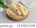 Stack of lavash or chapati flatbreads on a wooden cutting board, with a jar of flour, fresh basil 143481106