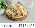 Stack of lavash or chapati flatbreads on a wooden cutting board, with a jar of flour, fresh basil 143481107