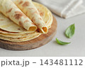 Stack of lavash or chapati flatbreads on a wooden cutting board, with a jar of flour, fresh basil 143481112