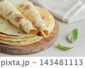 Stack of lavash or chapati flatbreads on a wooden cutting board, with a jar of flour, fresh basil 143481113