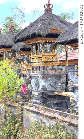Balinese Hindu temple pavilions rise in cluster, combining carved gray stone with intricate gold ornament. Thatched roofs, crown shaped finials and painted deity panels create richly detailed sacred 143482021