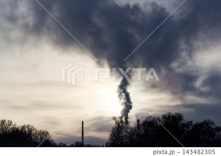 Dense plumes of steam billow from industrial chimneys into the cold winter sky, casting a dramatic dark cloud over the frost-covered landscape during a frosty morning Dense plumes of steam billow from industrial chimneys into the cold winter sky, casting a dramatic dark cloud over the frost-covered landscape during a frosty morning 143482305