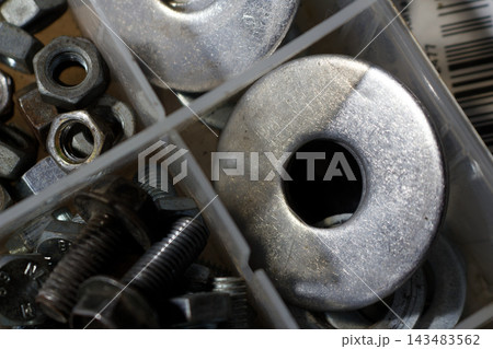 Close-up view of industrial metal washers and hex nuts organized in a transparent plastic storage box, perfect for DIY construction projects and professional repair maintenance tasks 143483562