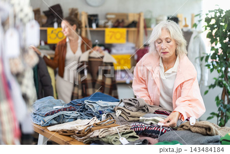 Senior woman customer examine and choose sweater in store. Other buyer in background, crowded shop 143484184