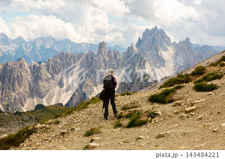 Tourist enjoying view of rocky peaks of Dolomites under cloudy sky 143484221