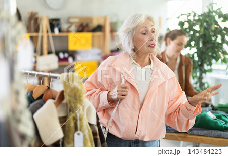 Elderly woman chooses outerwear in store 143484223