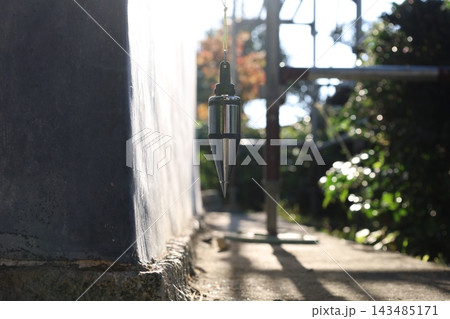 秋の紅葉を背景に外壁沿いに吊るされた下げ振りの建築測量 143485171