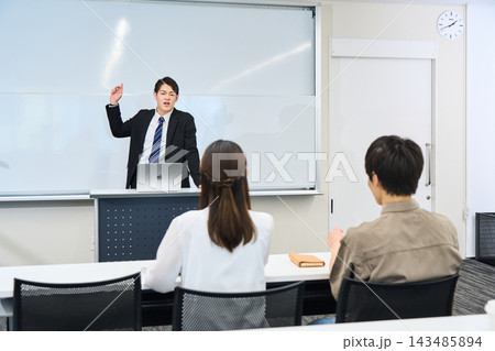 教室で熱心に講義を行うスーツ姿の男性講師と受講生 教室で熱心に講義を行うスーツ姿の男性講師と受講生 143485894
