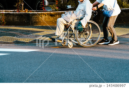 高齢者の奥さんが夫の車椅子を押して横断歩道を渡る 高齢者の奥さんが夫の車椅子を押して横断歩道を渡る 143486997