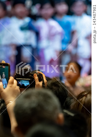 Parents recording their children school performance with camera, audience engagement at a school event 143487981