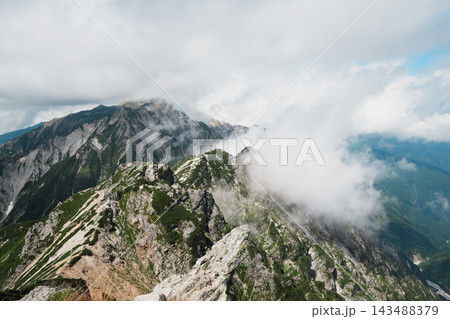 岩稜の山並みを越えて谷へ流れ込む白い雲 岩稜の山並みを越えて谷へ流れ込む白い雲 143488379
