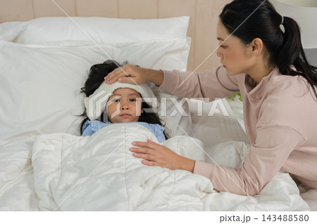 mother applying cold compress on sick daughter's forehead in bed 143488580