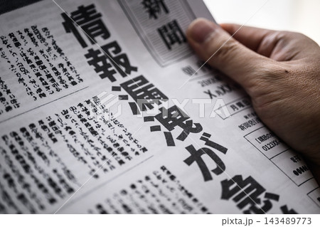 情報漏洩が危惧される新聞記事を指で押さえる手元 143489773