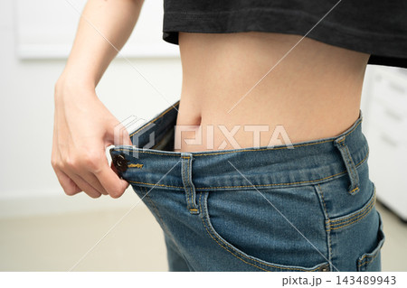 Young Asian woman losing weight wearing loose pants in oversize jeans. 143489943